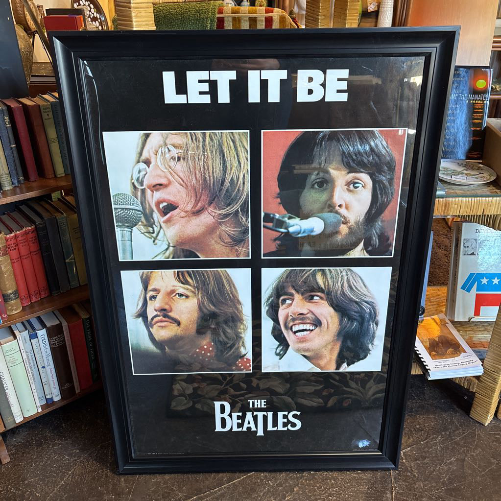 A black framed poster of the Beatles' album Let It Be leaning against a bookcase.