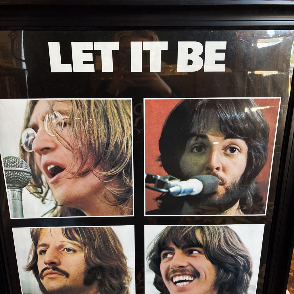 A black framed poster of the Beatles' album Let It Be leaning against a bookcase.