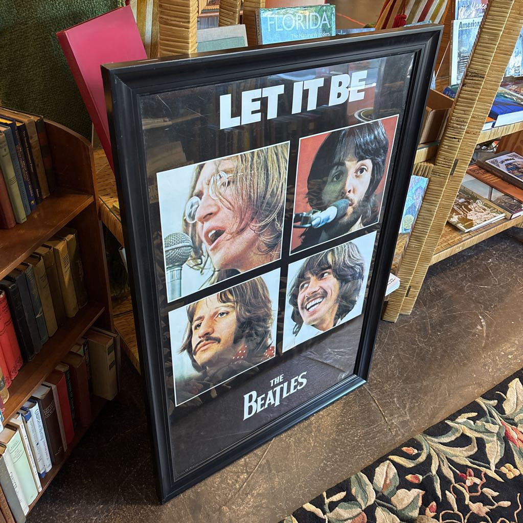 A black framed poster of the Beatles' album Let It Be leaning against a bookcase.
