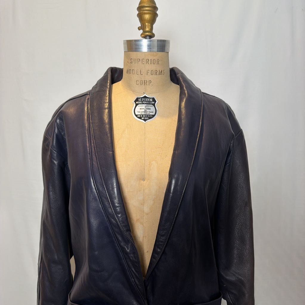A navy leather trench jacket on a mannequin in front of a white wall.