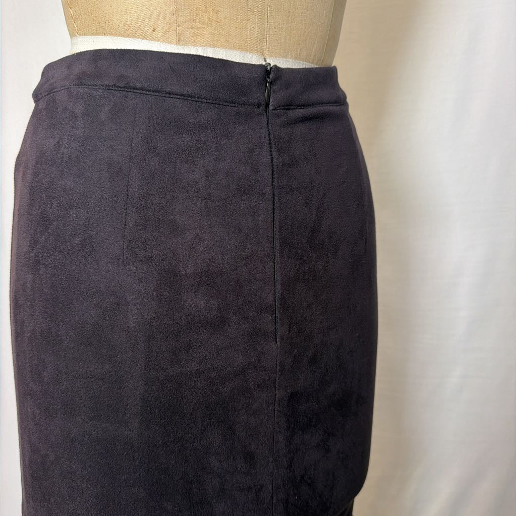 A black high-waisted skirt with a long fringe hem on a mannequin in front of a white wall.