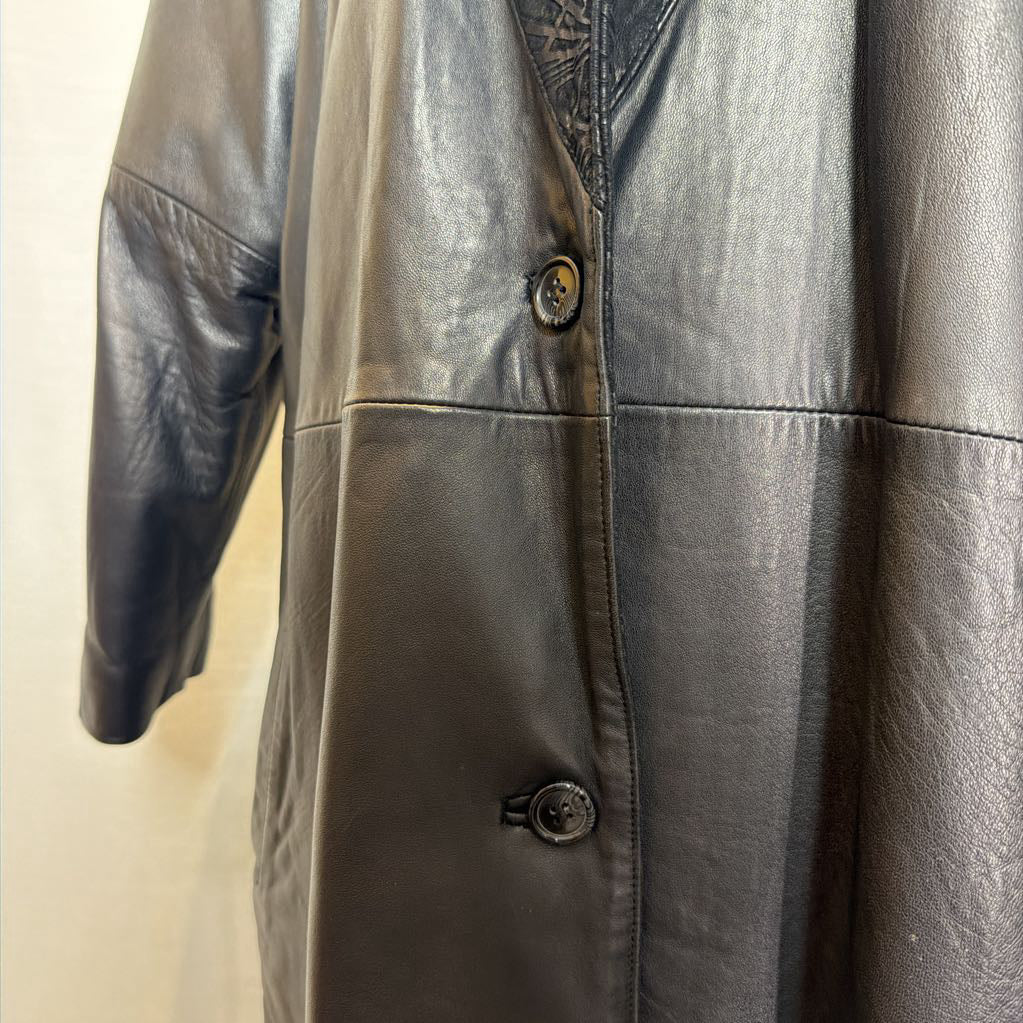 A black leather trench coat with wide shoulders and an abstract design on the lapels. Its on a mannequin in front of a white wall.