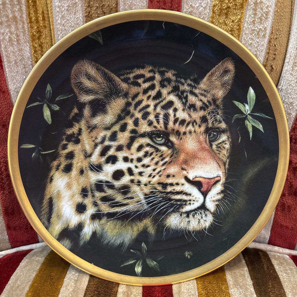 A painted leopard on a black and gold decorative plate sitting on a red and gold striped cushion.