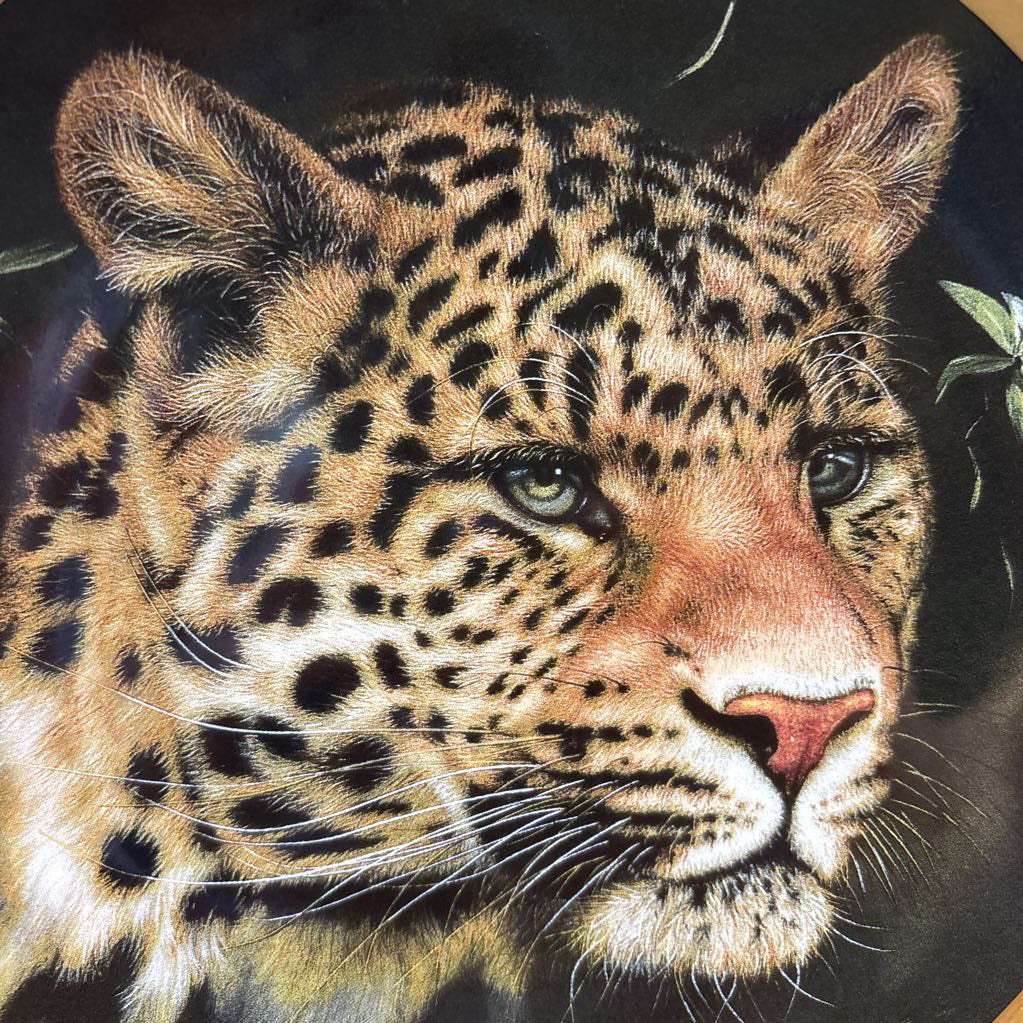 A painted leopard on a black and gold decorative plate sitting on a red and gold striped cushion.