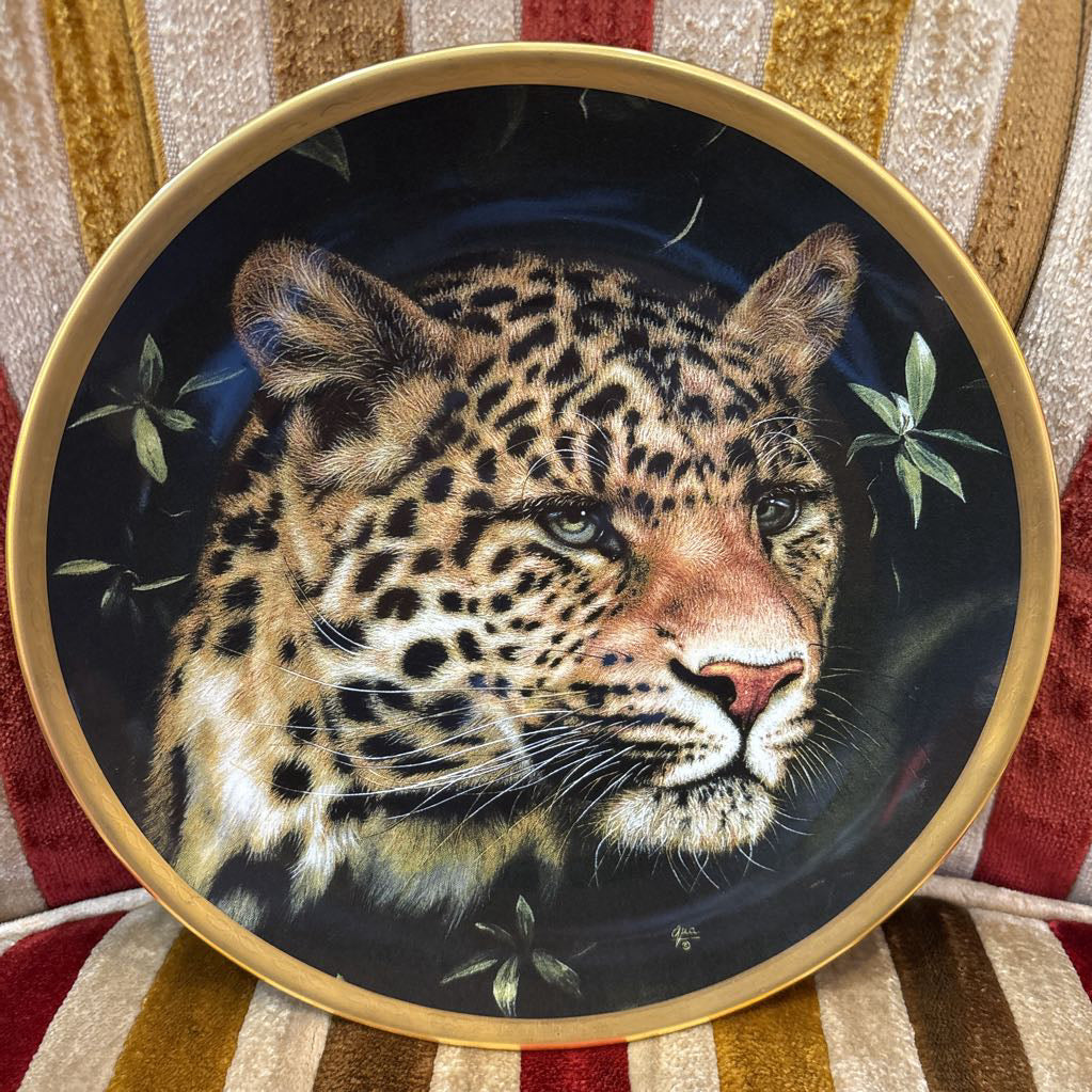 A painted leopard on a black and gold decorative plate sitting on a red and gold striped cushion.