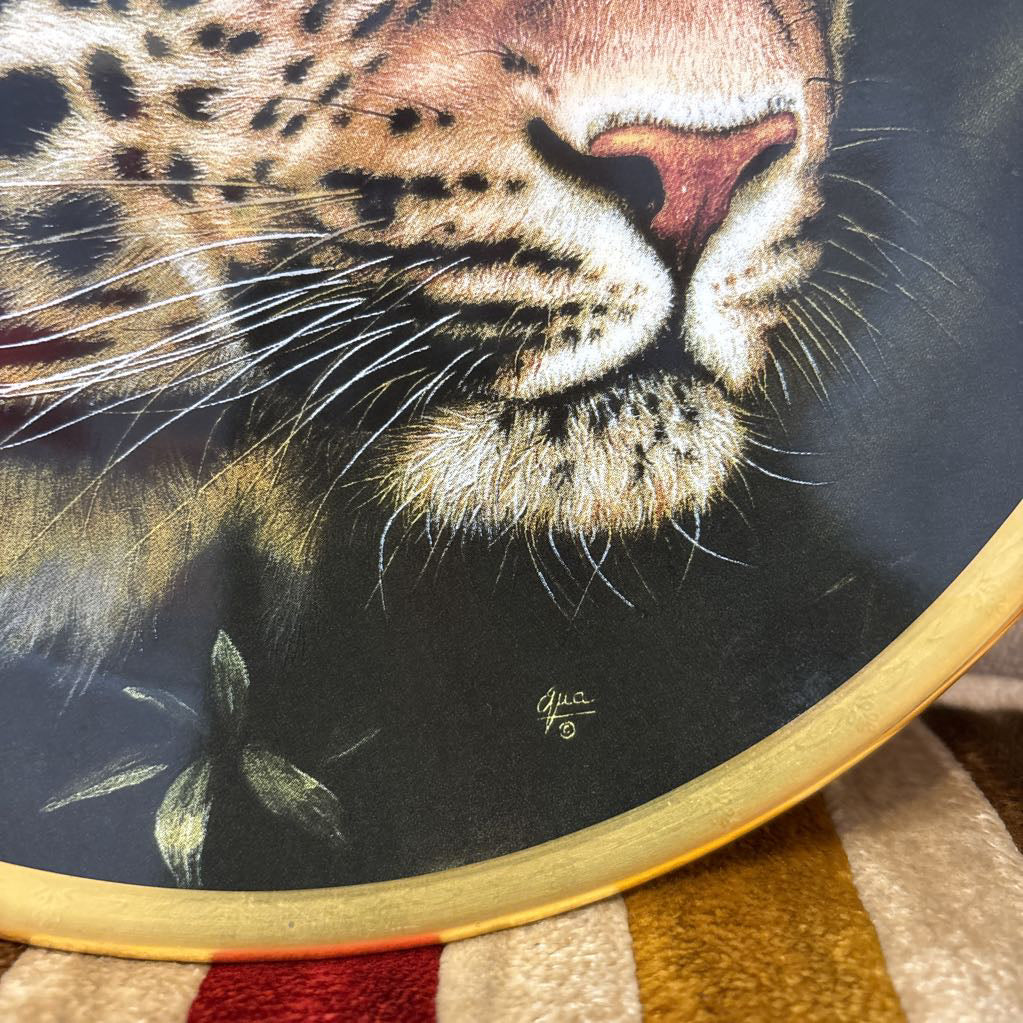 A painted leopard on a black and gold decorative plate sitting on a red and gold striped cushion.