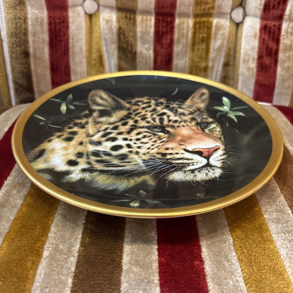 A painted leopard on a black and gold decorative plate sitting on a red and gold striped cushion.