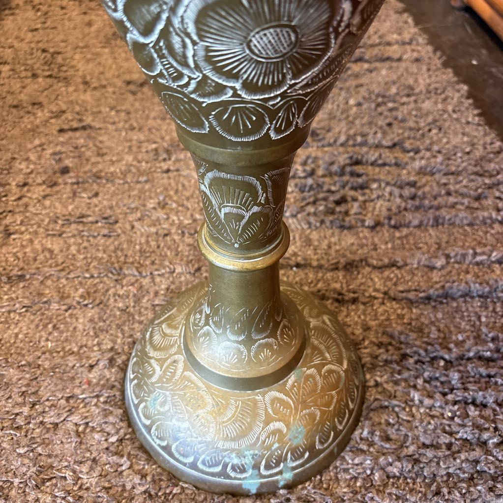 A large, engraved brass vase on a rug in a room setting.