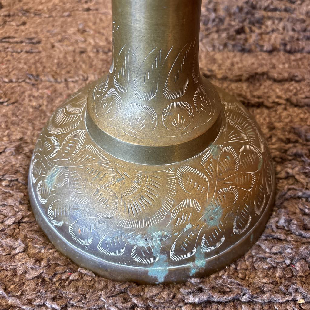 A large, engraved brass vase on a rug in a room setting.