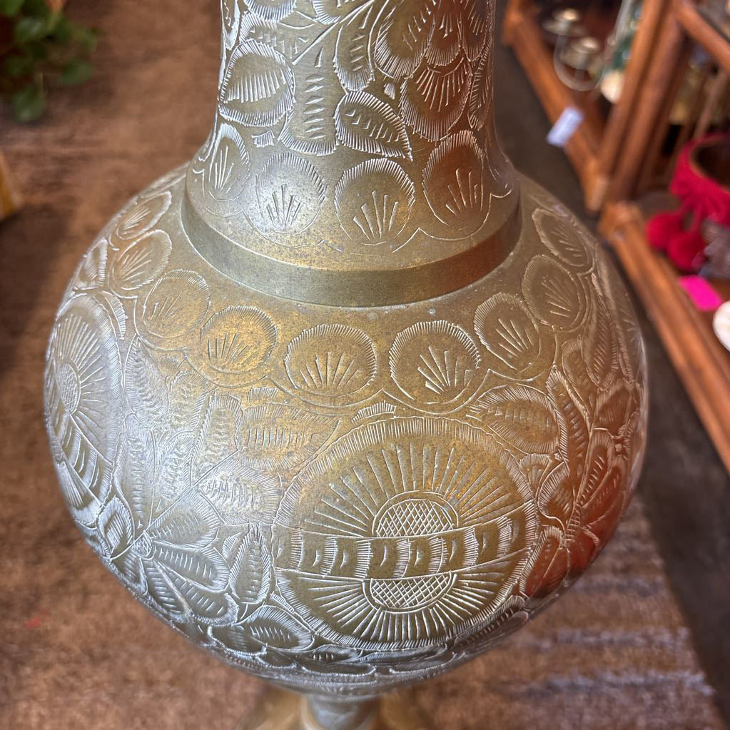 A large, engraved brass vase on a rug in a room setting.