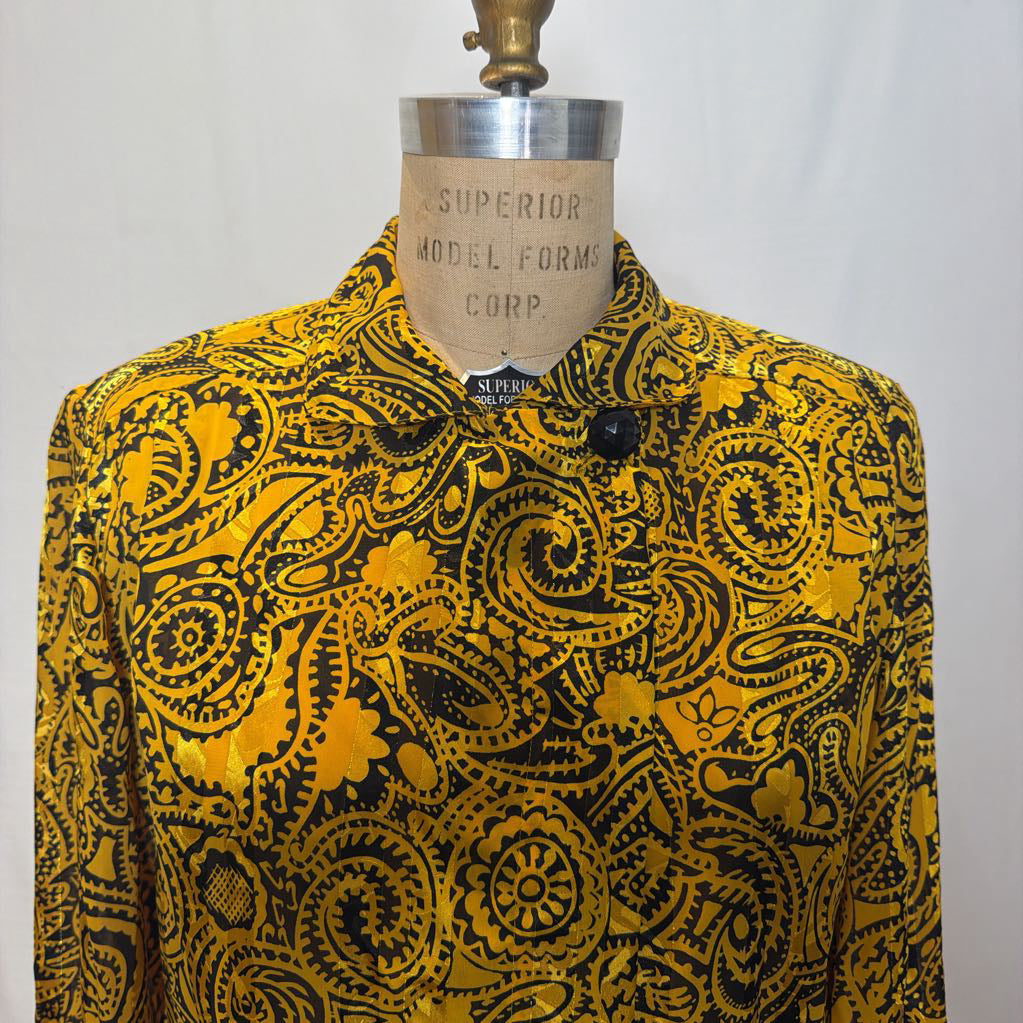 A yellow and black paisley patterned blouse on a mannequin in front of a white wall.