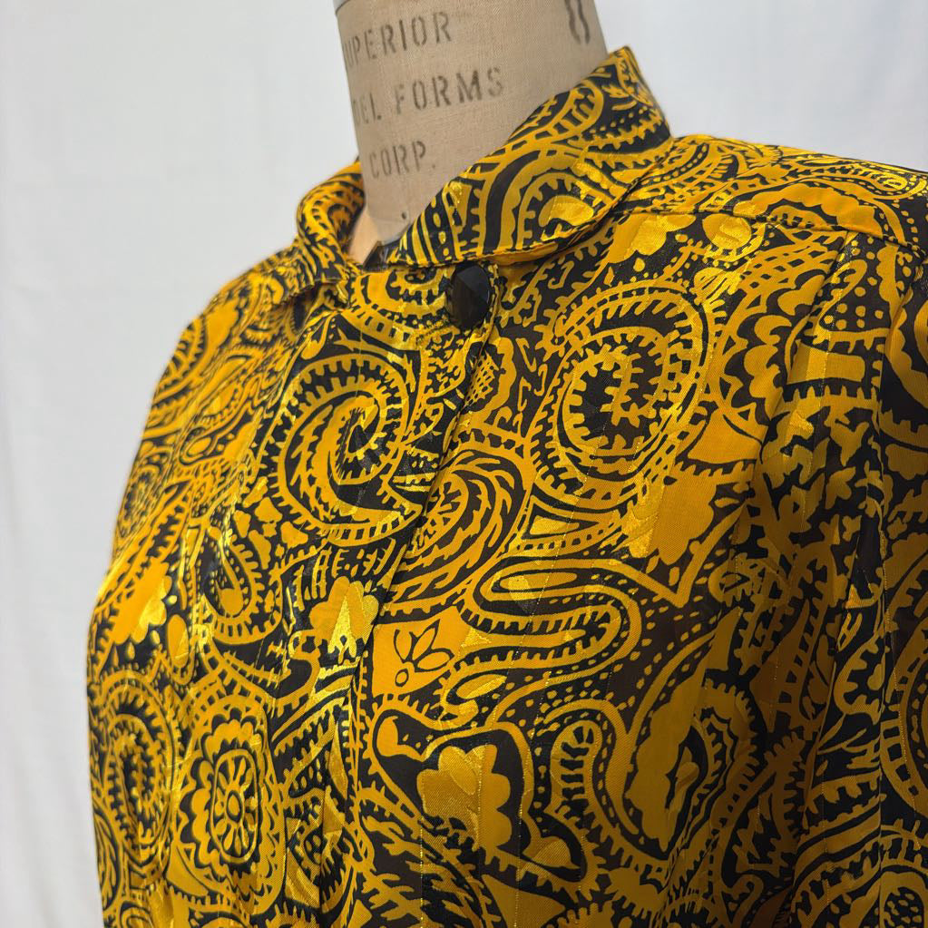 A yellow and black paisley patterned blouse on a mannequin in front of a white wall.