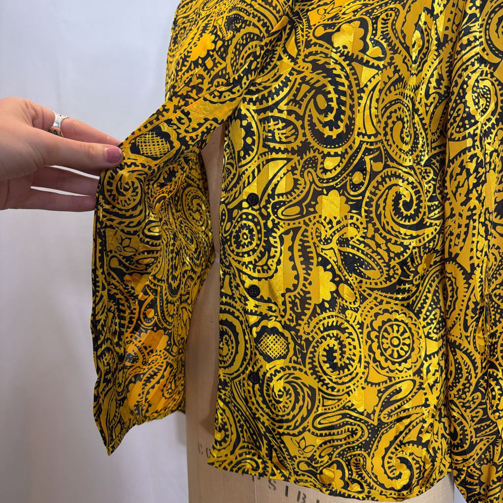 A yellow and black paisley patterned blouse on a mannequin in front of a white wall.