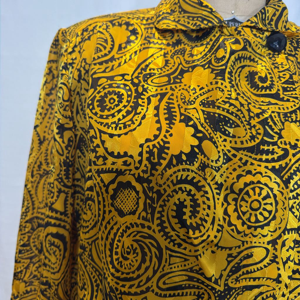A yellow and black paisley patterned blouse on a mannequin in front of a white wall.