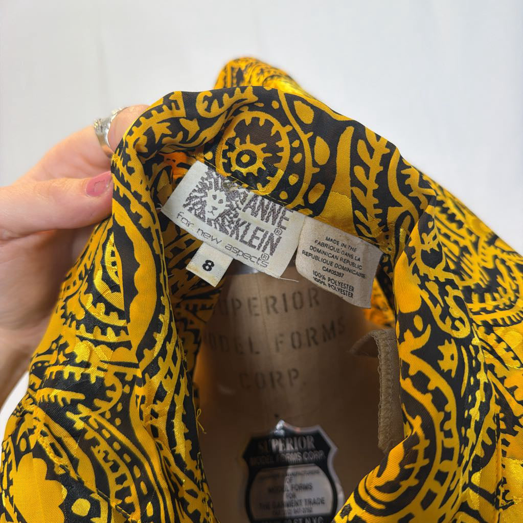 A yellow and black paisley patterned blouse on a mannequin in front of a white wall.