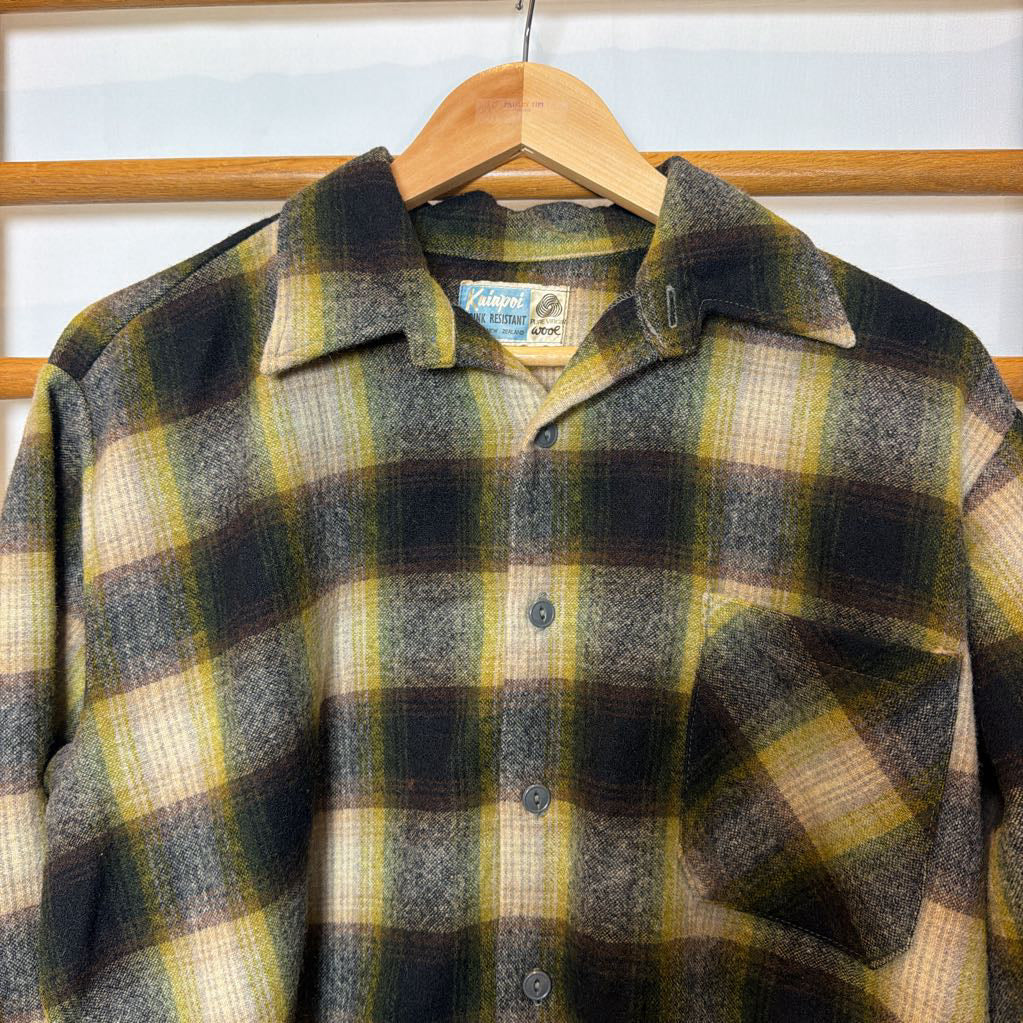 A green ombre plaid button-up shirt on a wooden rack.