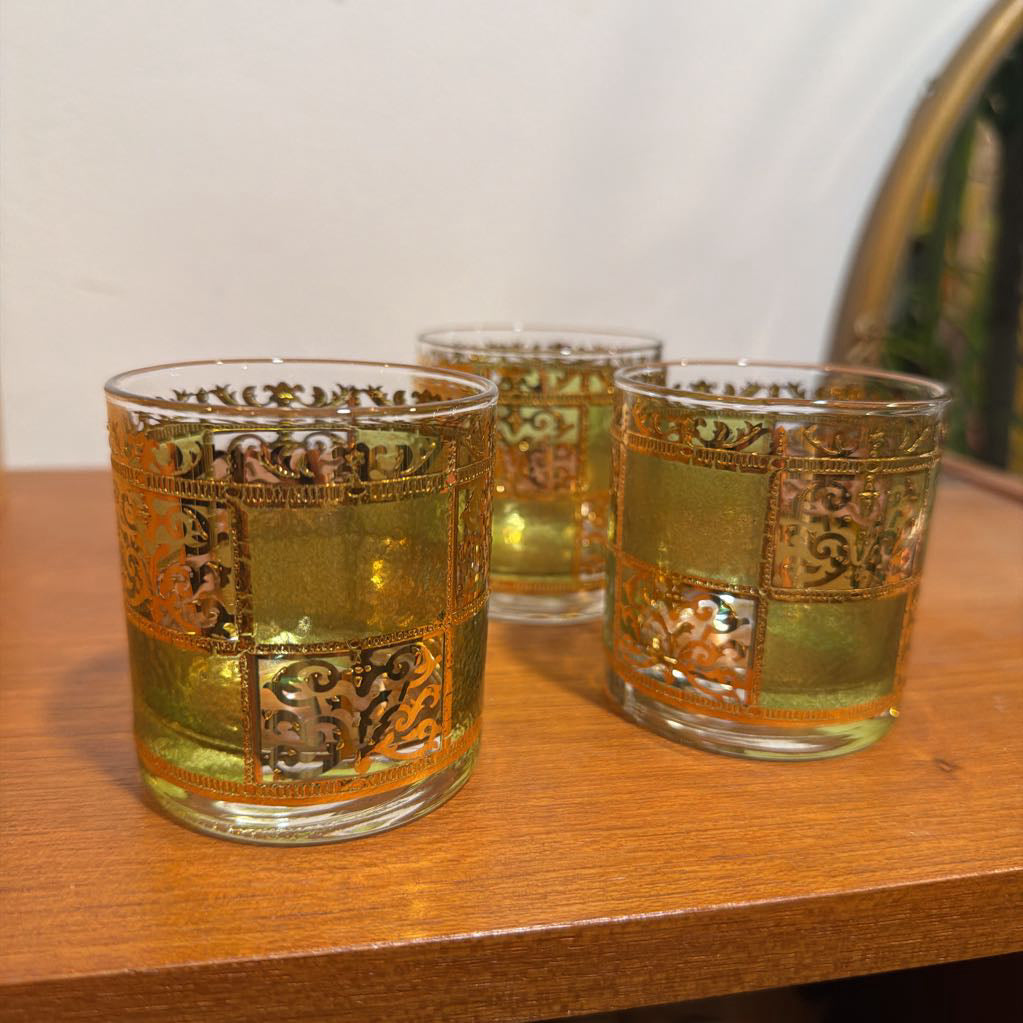 Three culver prado green glassware featuring a pale green tine and ornate 22k gold filigree checkerboard panels sitting on wood.