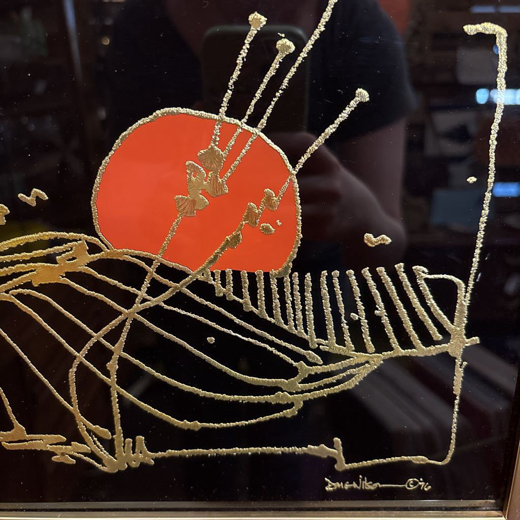 A black glossy artwork with textured gold linework and an orange circle. This piece is hanging on an orange fabric overed wall.
