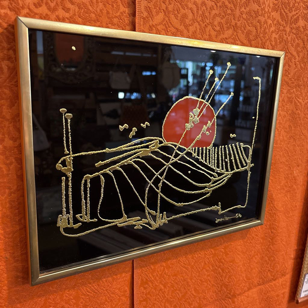 A black glossy artwork with textured gold linework and an orange circle. This piece is hanging on an orange fabric overed wall.