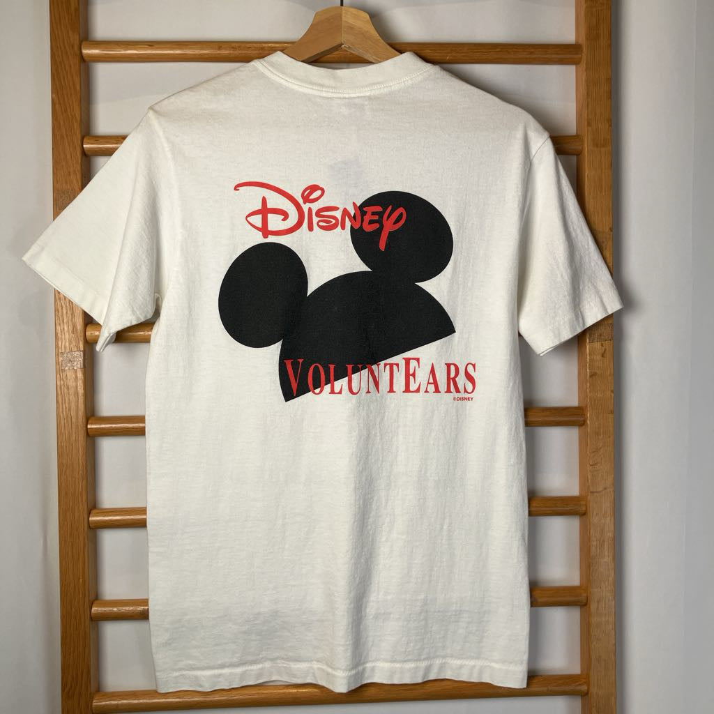 White t-shirt with Disney VoluntEARS design on a wooden hanger against a white wall.