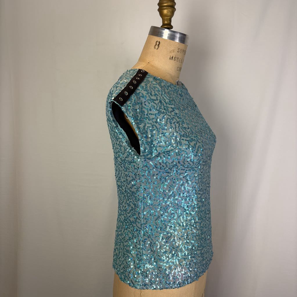A turquoise blue sequined short-sleeve top displayed on a vintage dress form mannequin against a neutral off-white background.