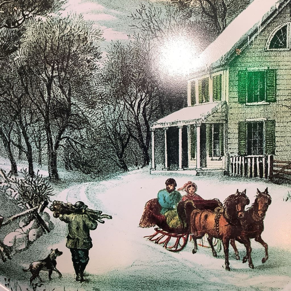 Winter scene with people on a horse-drawn sleigh in front of a house.