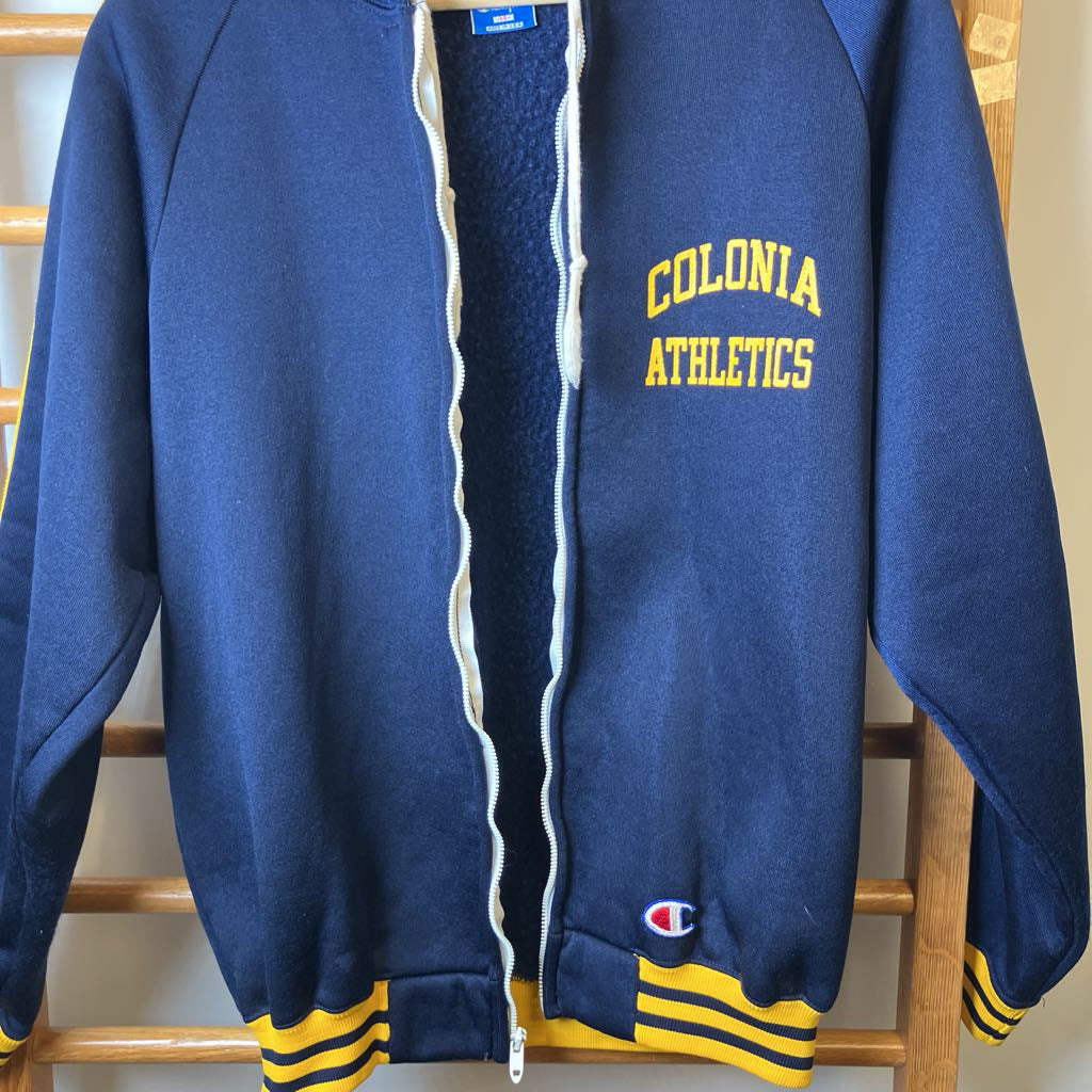 Blue jacket with 'Colonia Athletics' text on a wooden rack