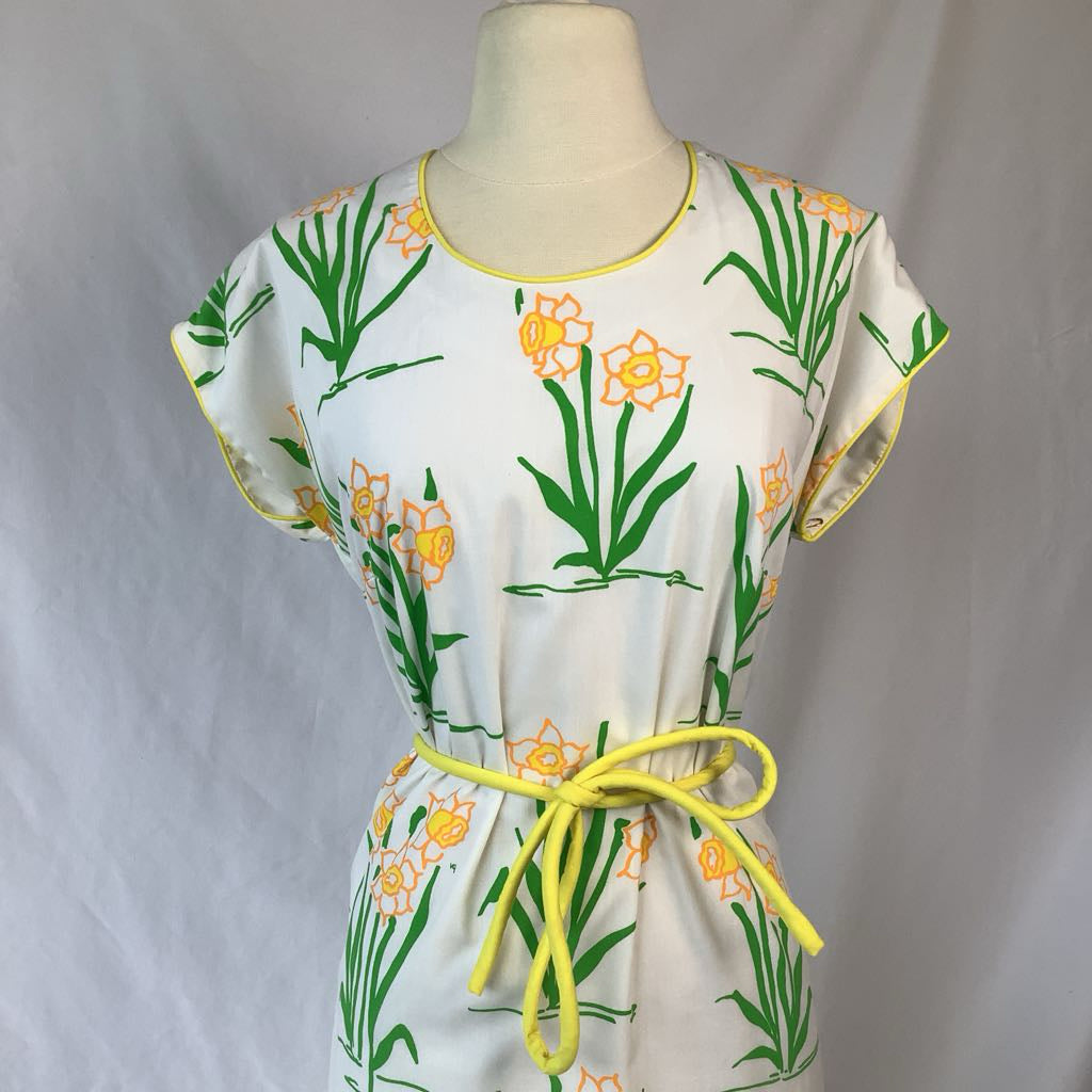 White dress with floral pattern and yellow tie on a mannequin against a gray background