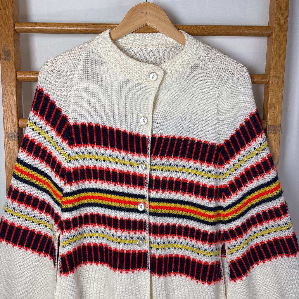 A white striped knitted poncho hanging on a wooden rack. 