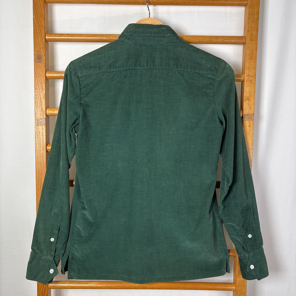 A green corduroy button-up long sleeve shirt on a wooden rack against a white wall. 