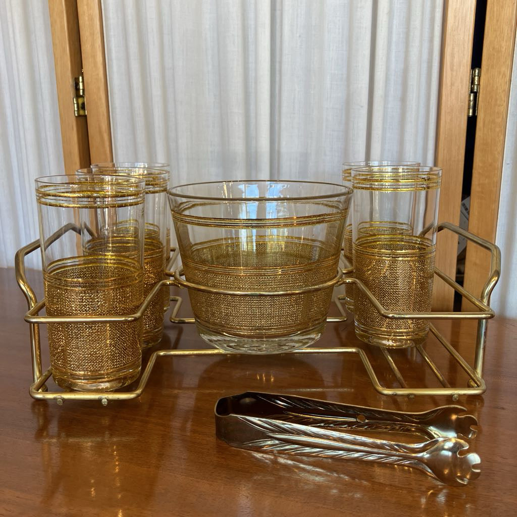 Set of gold-detailed glasses on a metal tray with a pair of tongs in front of it