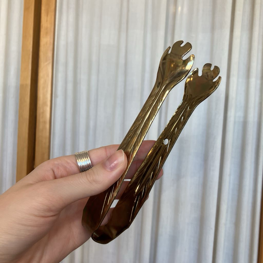Hand holding a pair of gold metal tongs against a white background