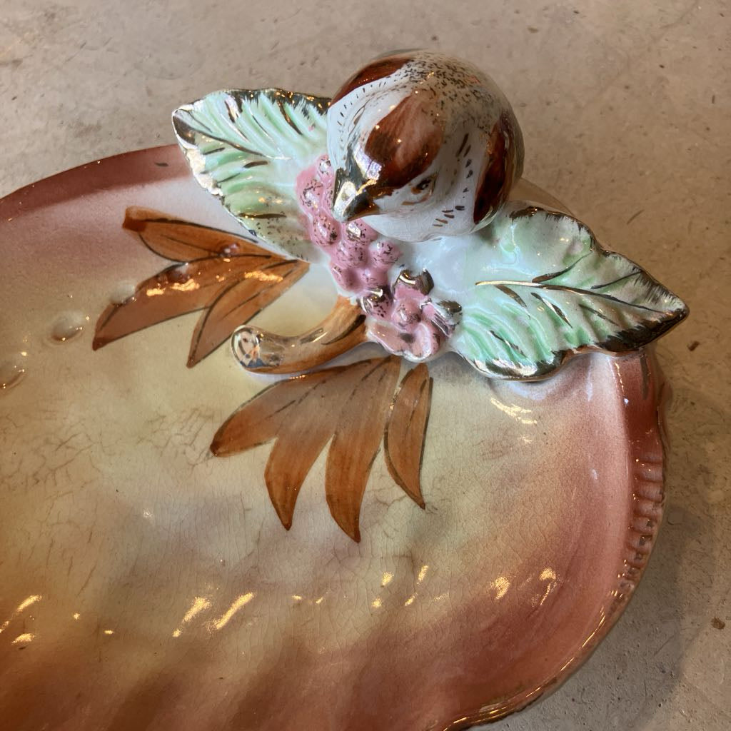 Over head view of decorative ceramic dish with a bird and floral design on a shell shaped base