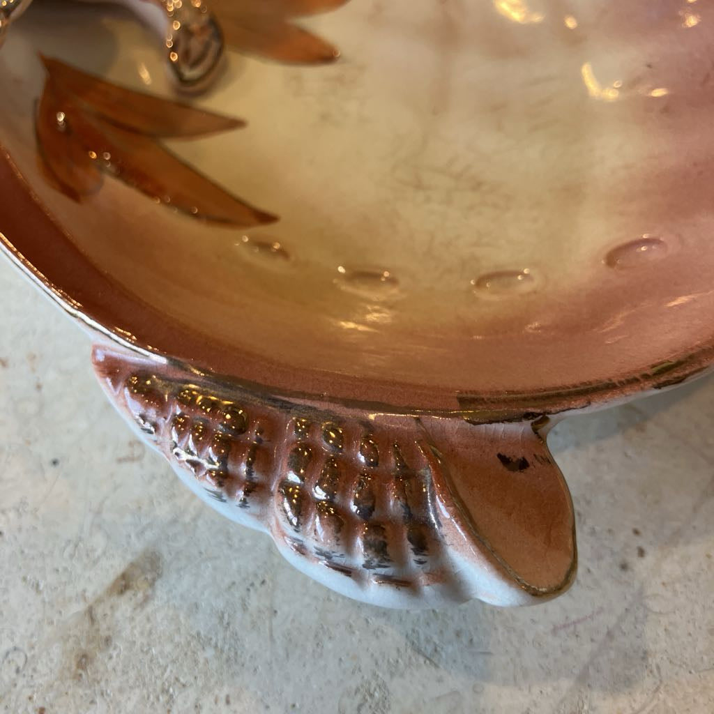 Close-up of a ceramic shell-shaped dish with decorative patterns on a textured surface