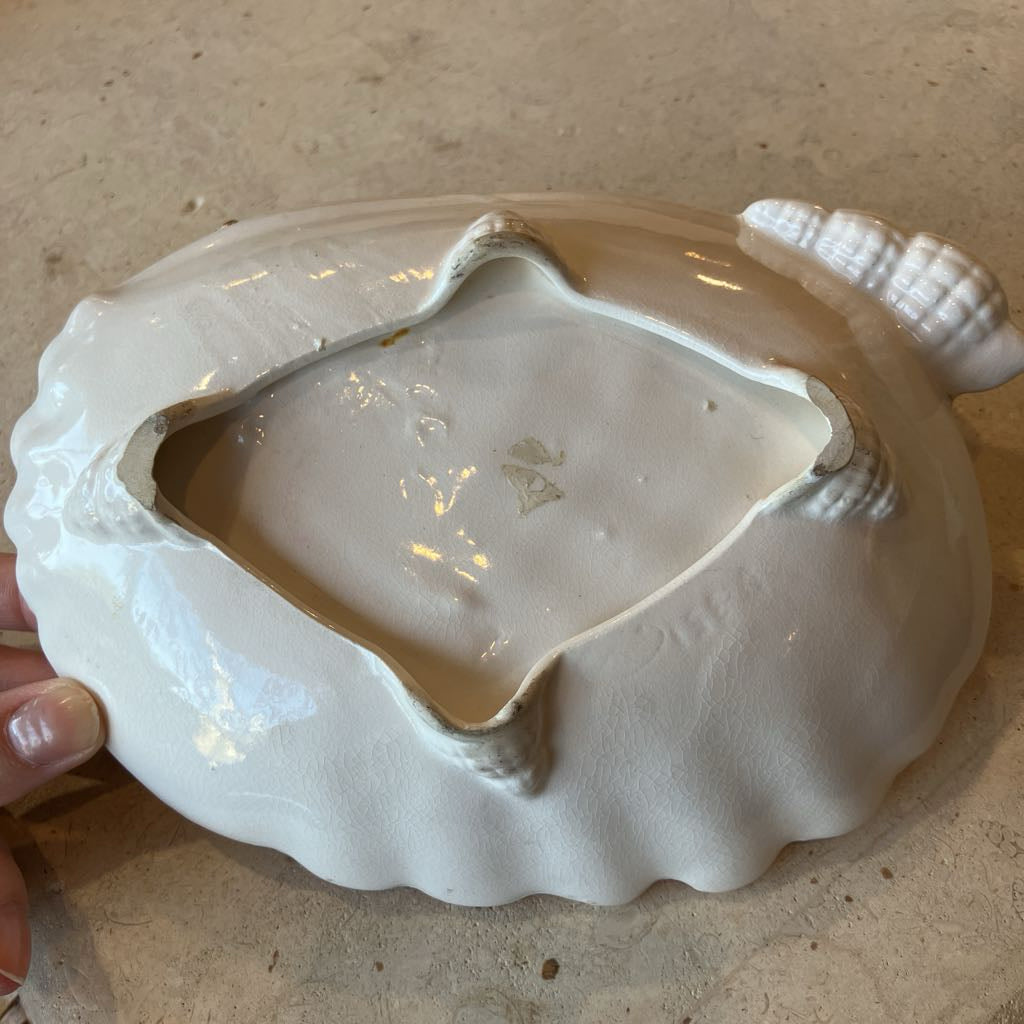 Bottom of white ceramic shell-shaped dish held by a hand on a beige surface