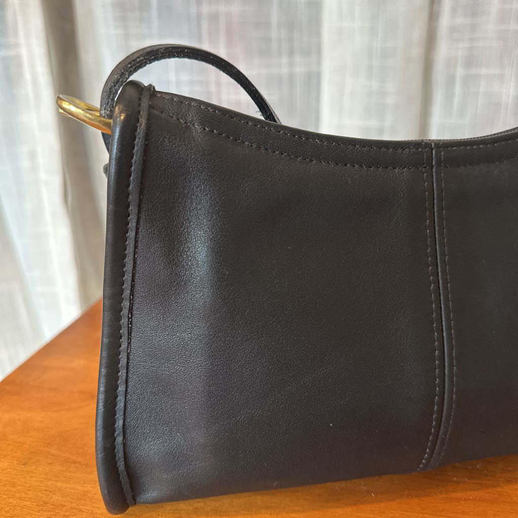 Black leather handbag on a wooden surface with a white curtain background