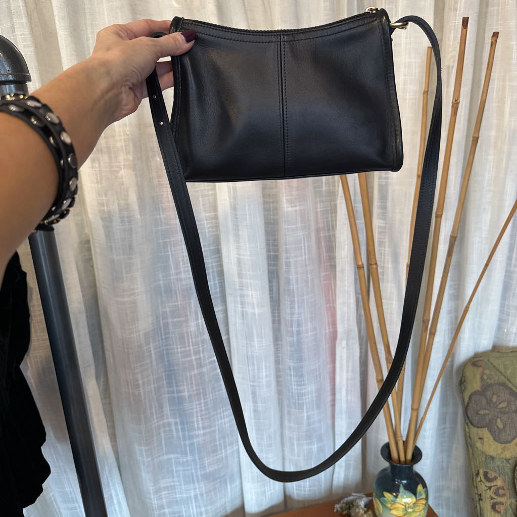 Person holding a black leather handbag with a plain background