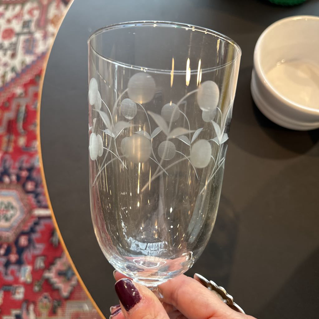 Clear glass with floral etching held by a hand on a dark surface.