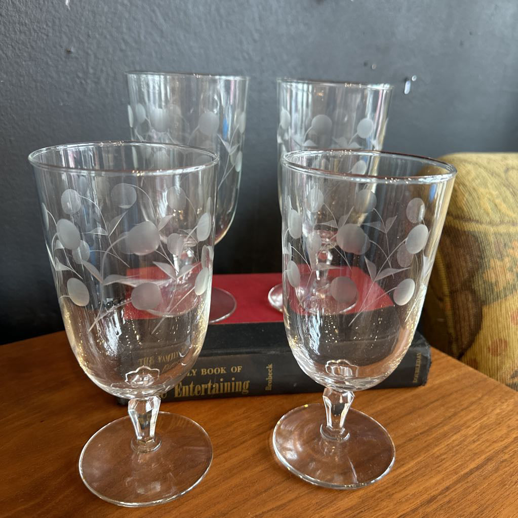 Four etched glass goblets on a wooden surface with books in the background.