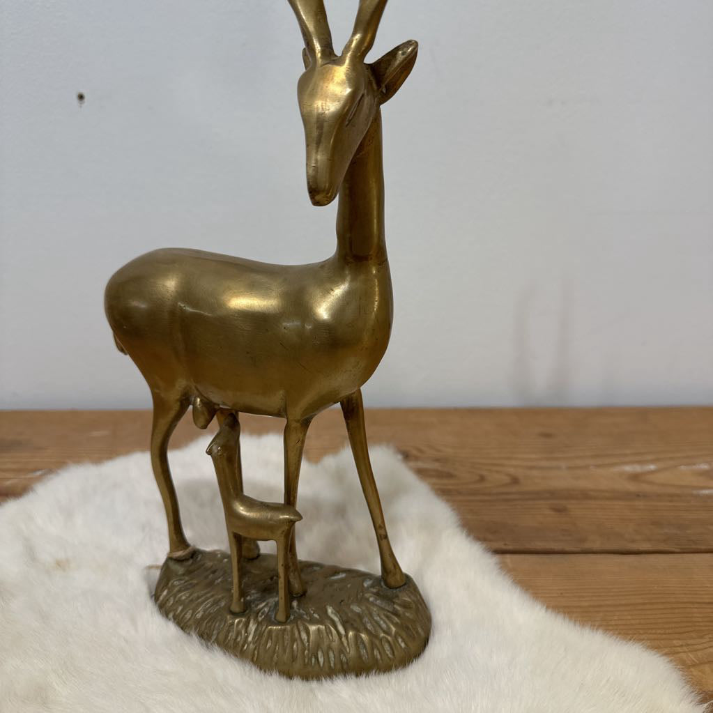 Bronze deer figurine on a white fur-like surface with a wooden floor and light gray wall background.