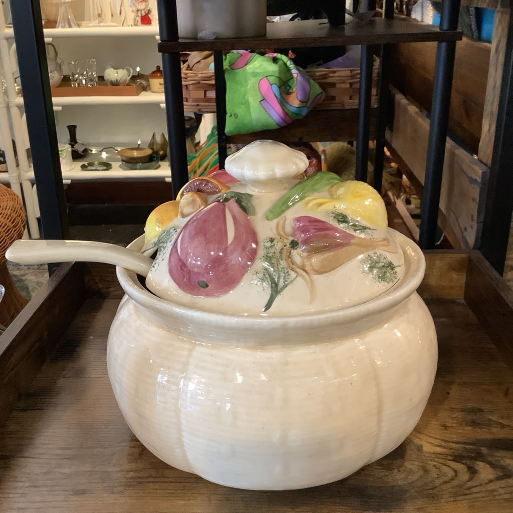 Decorative ceramic pot with lid featuring fruit designs on a wooden surface.