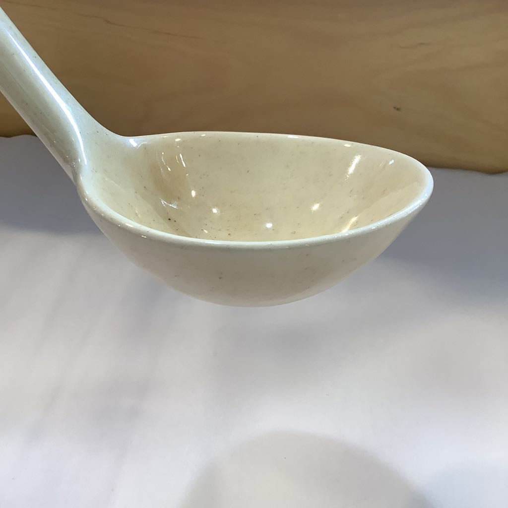 White ceramic spoon on a white surface with a wooden background