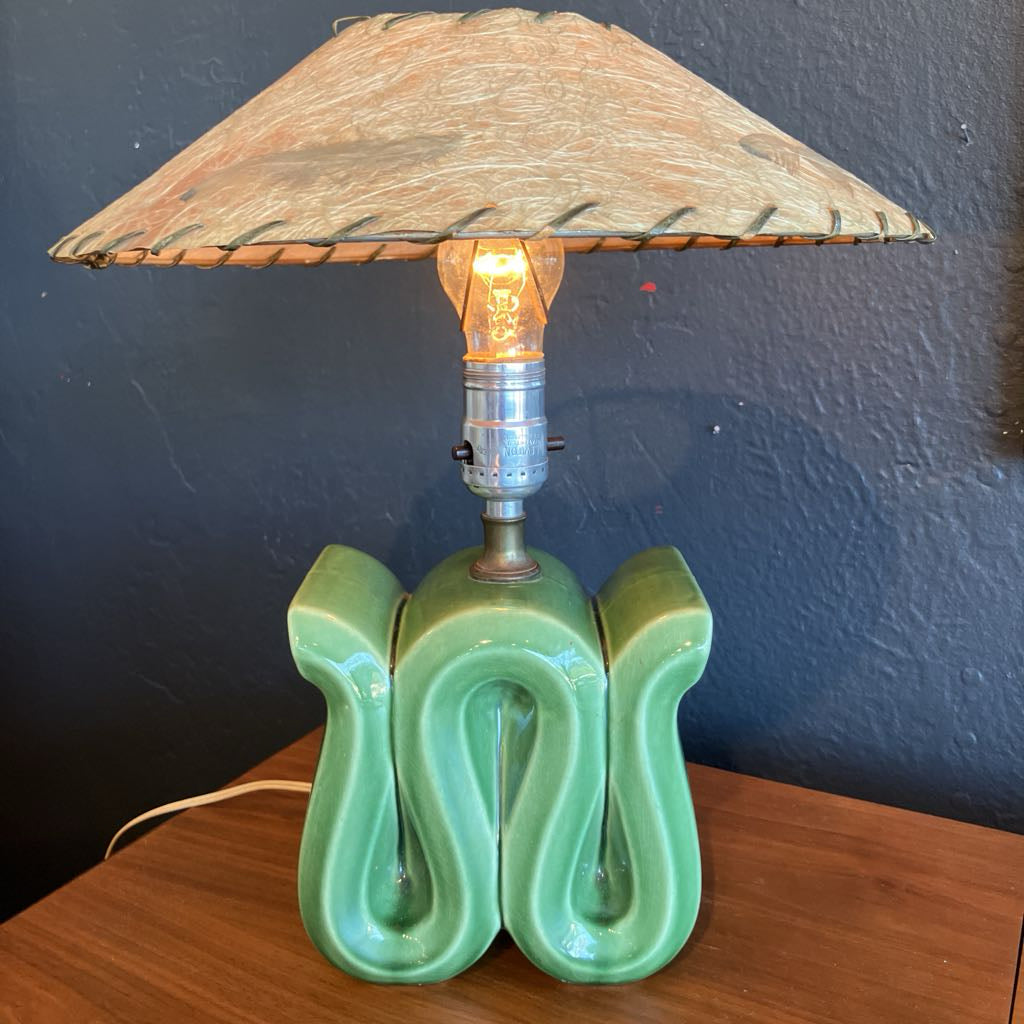 Green squiggly shape lamp base with brown fiberglass lamp shade on a wooden surface and with black background