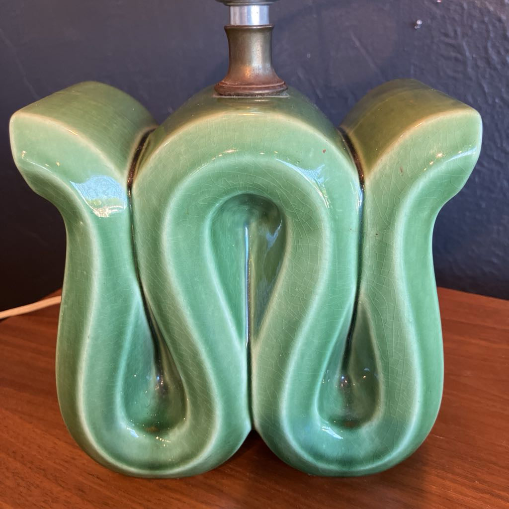 Green squiggly shape lamp base on a wooden surface and with black background