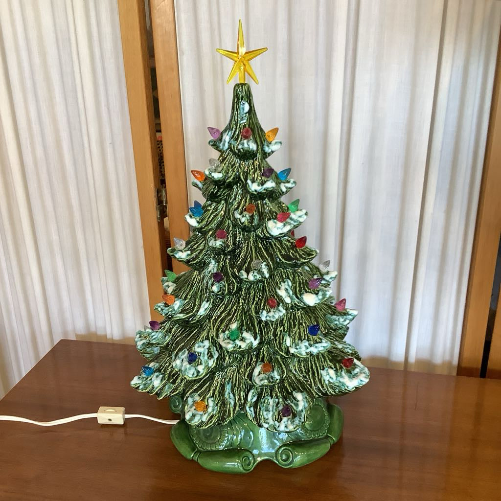 Decorative Christmas tree with colorful ornaments and a gold star on top, placed on a wooden surface.