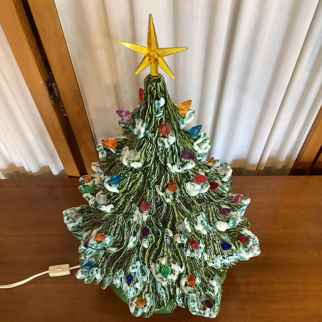 Decorative Christmas tree with lights and a star on top, placed on a wooden surface.