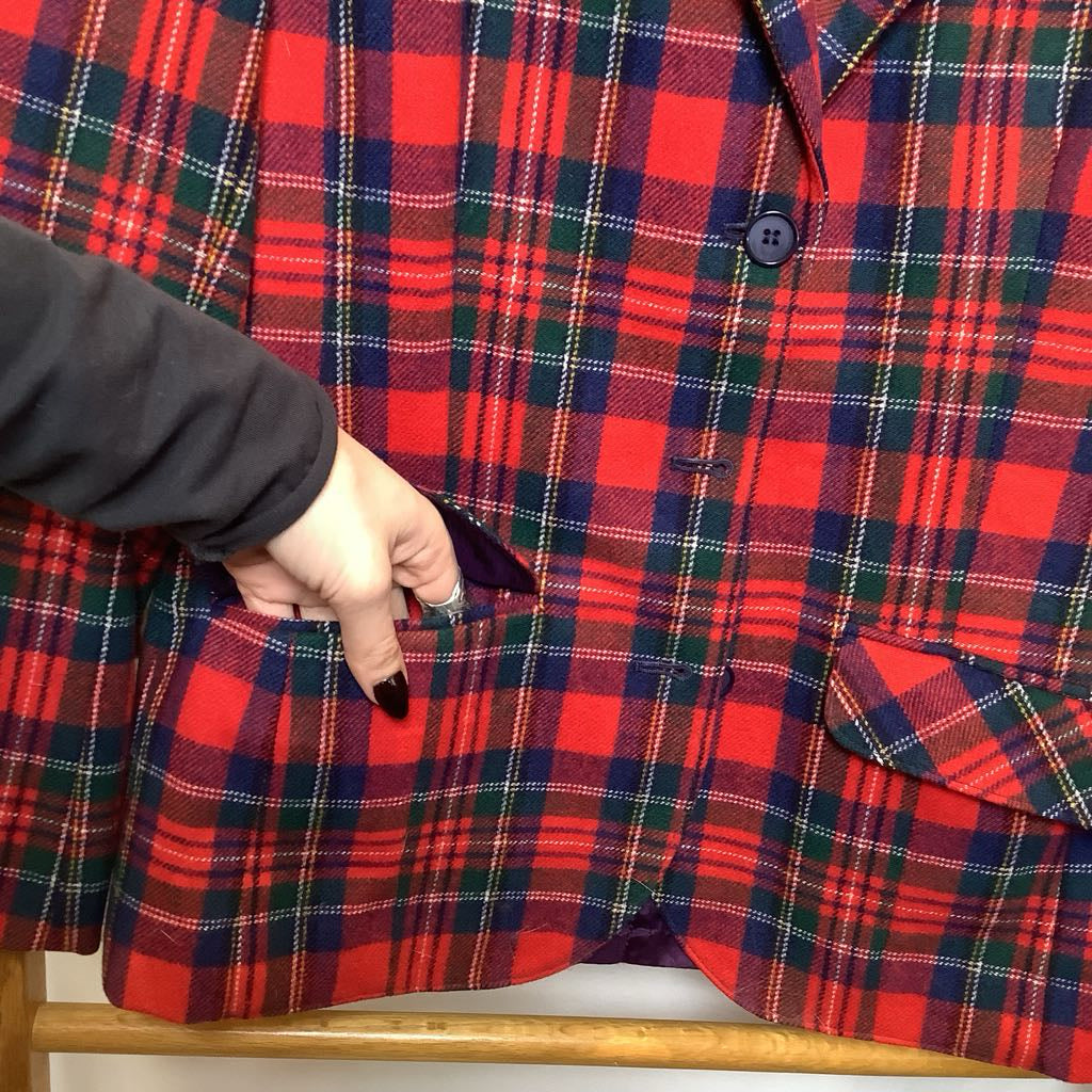 Red and green plaid shirt on a hanger with a hand adjusting it.