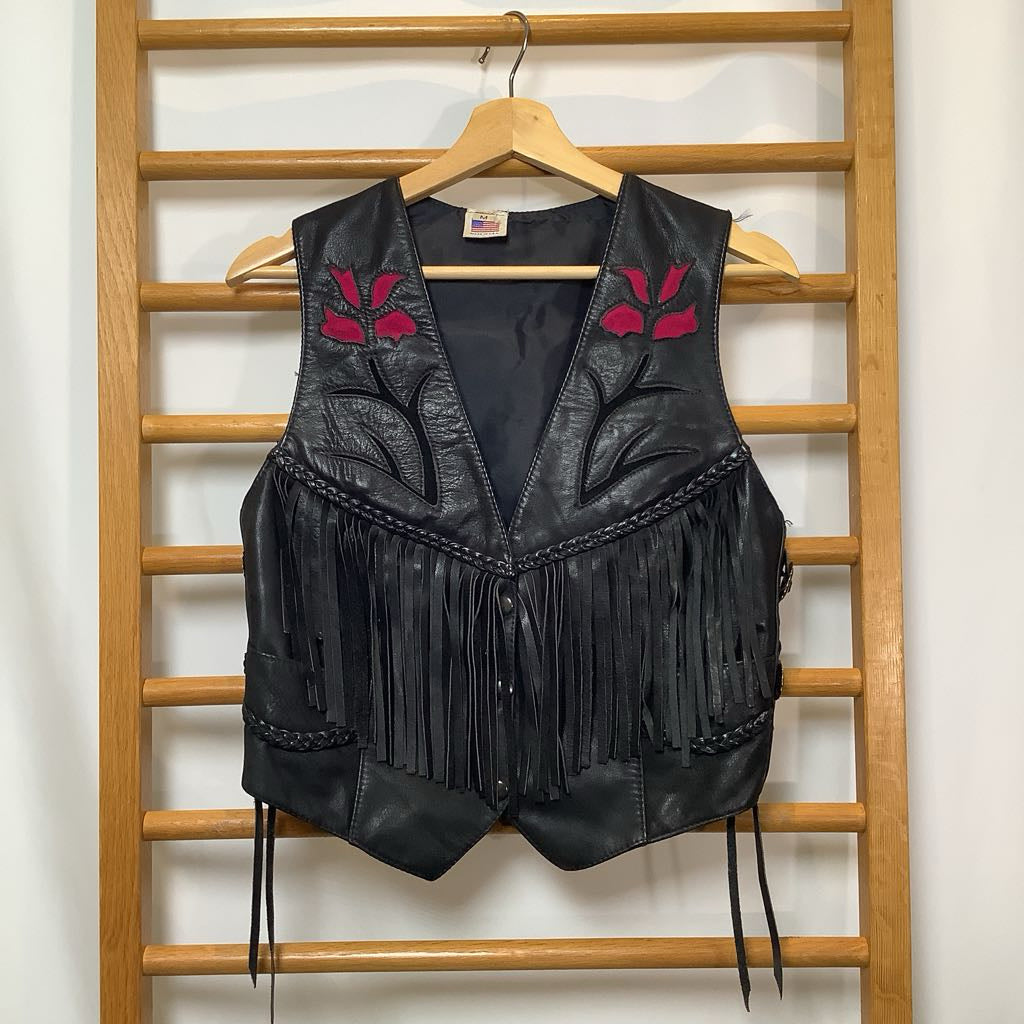 Black leather vest with fringe and floral embroidery on a wooden rack.