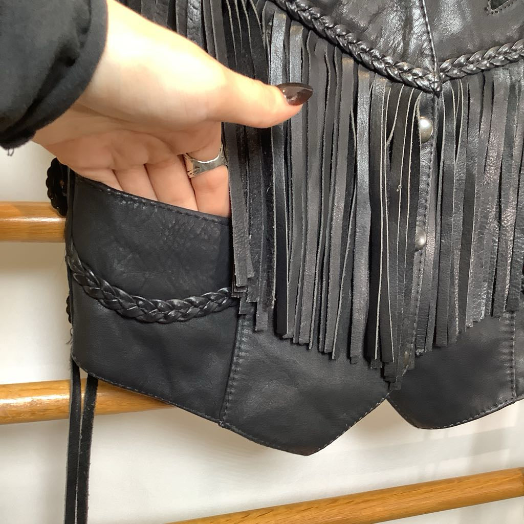 Black fringe bag held by a hand on a wooden surface