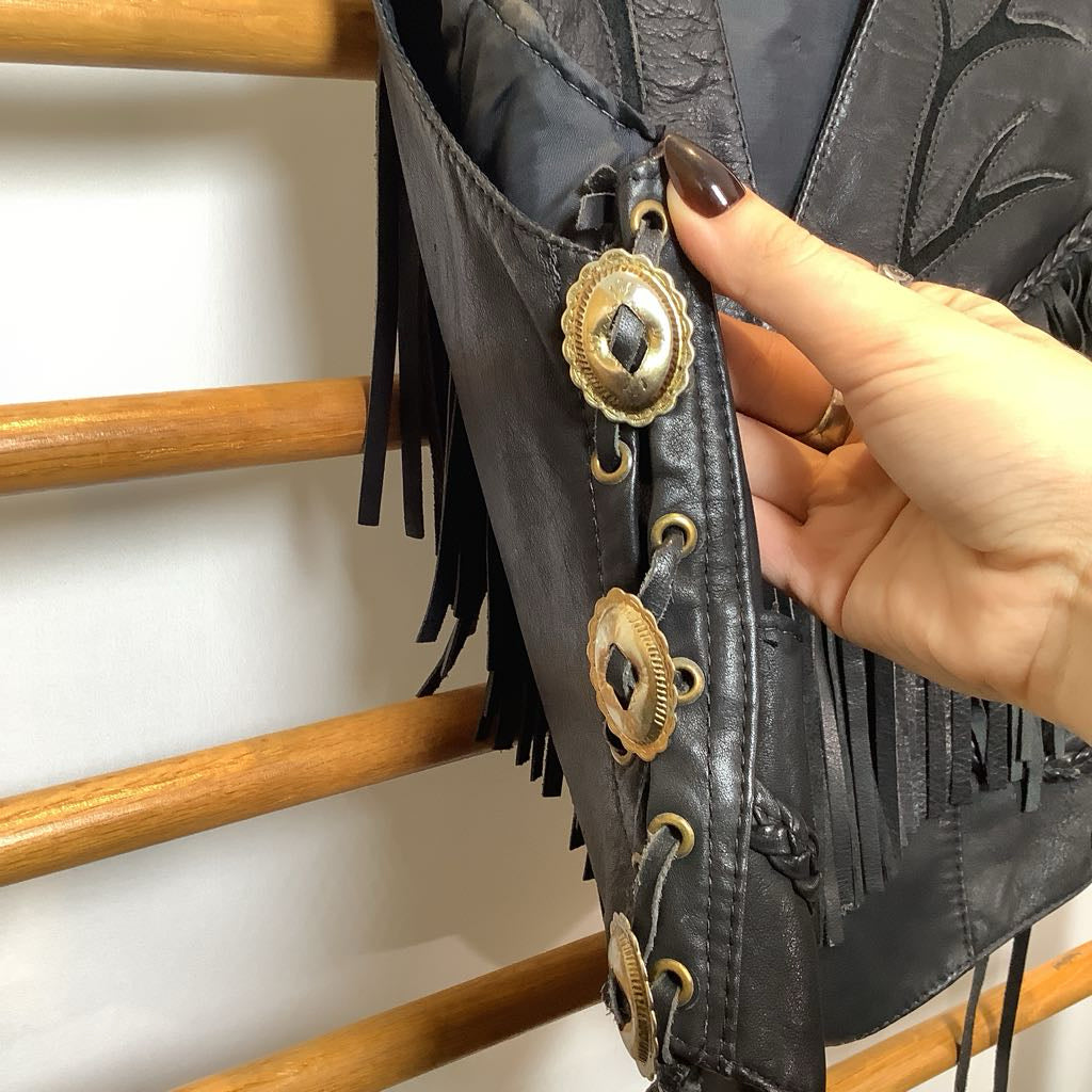 Black leather boot with gold decorative elements held by a hand against a wooden background